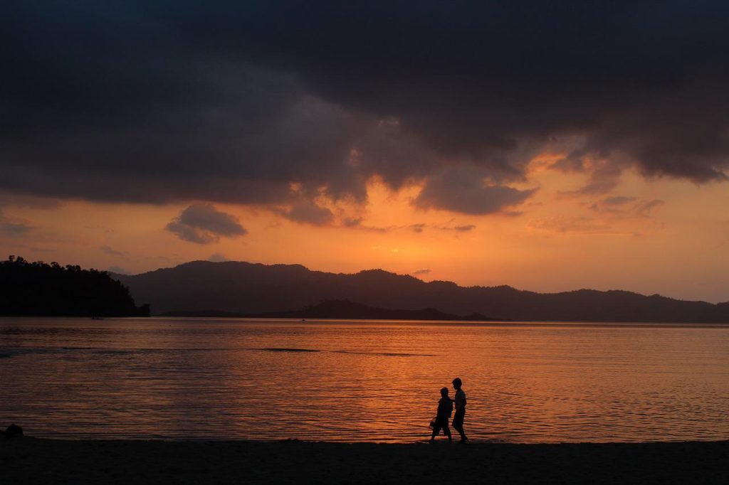 A beach with two visitors in the Philippines with mountains in the horizon.